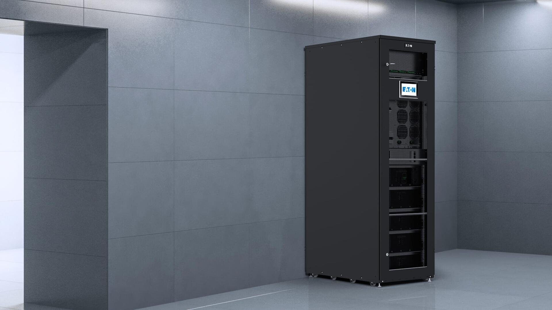 Ein hoher, schwarzer Serverschrank mit mehreren elektronischen Komponenten und einem digitalen Bildschirm steht vor einer grau gekachelten Wand in einem sauberen, modernen Raum.