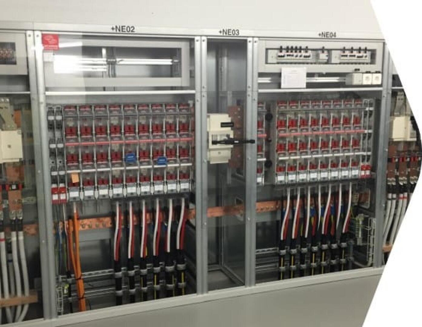 Drei elektrische Schalttafeln mit den Bezeichnungen NE02, NE03 und NE04, die jeweils mehrere Schalter, Leistungsschalter und farbige Kabel enthalten, die übersichtlich in Metallgehäusen untergebracht sind.
