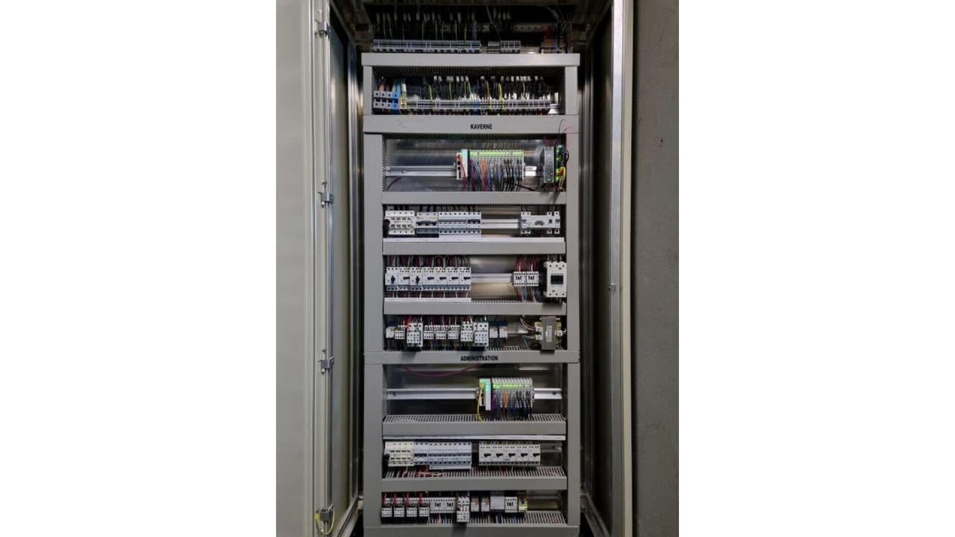 An open electrical control panel with multiple rows of circuit breakers, relays, wiring, and electronic components neatly organized inside a metal enclosure.