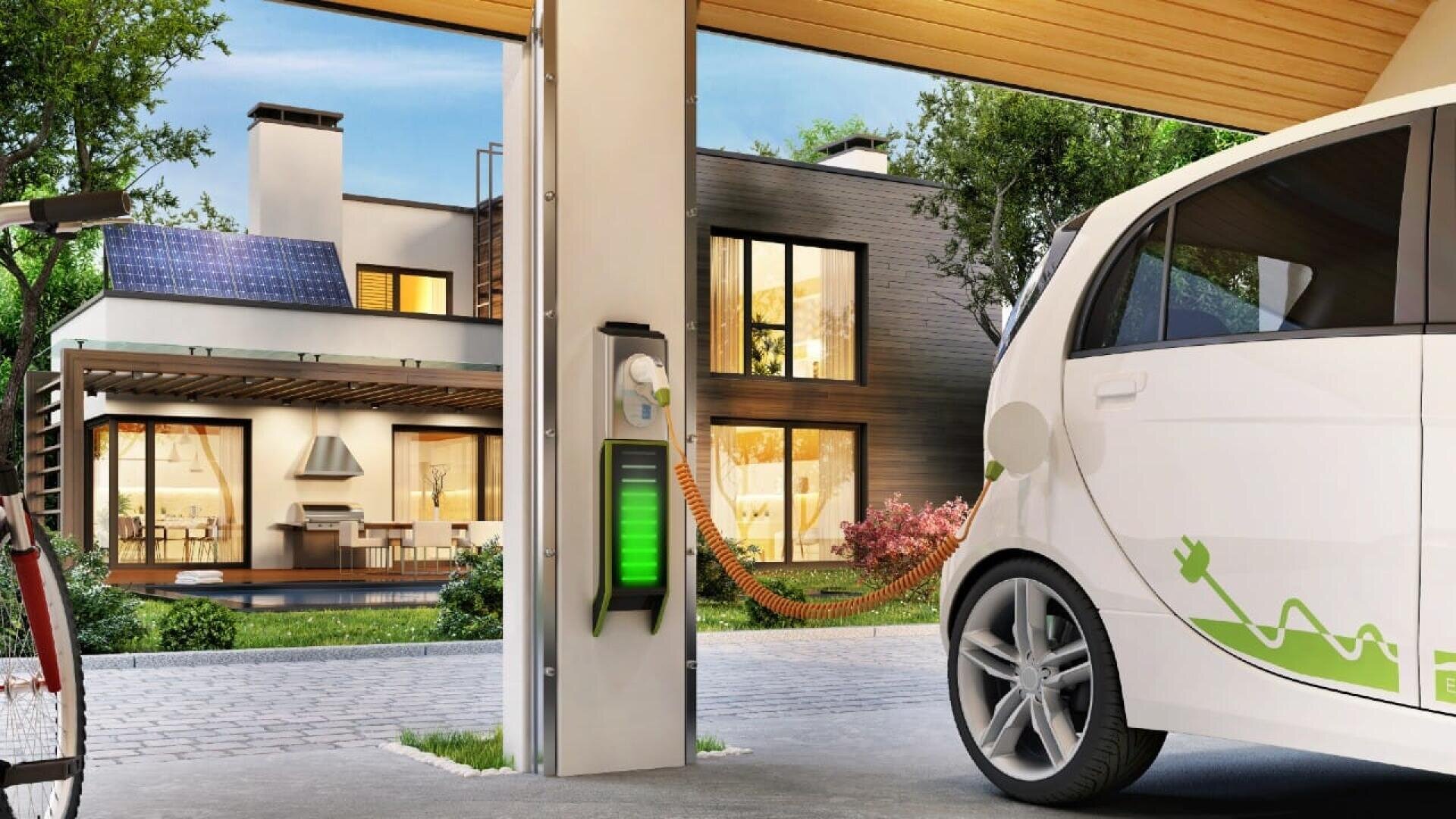 Ein weißes Elektroauto wird in der Einfahrt eines modernen Hauses aufgeladen. Das Haus verfügt über Sonnenkollektoren auf dem Dach, große Fenster und eine Hängematte im Garten, was auf einen umweltfreundlichen und nachhaltigen Lebensstil hindeutet.