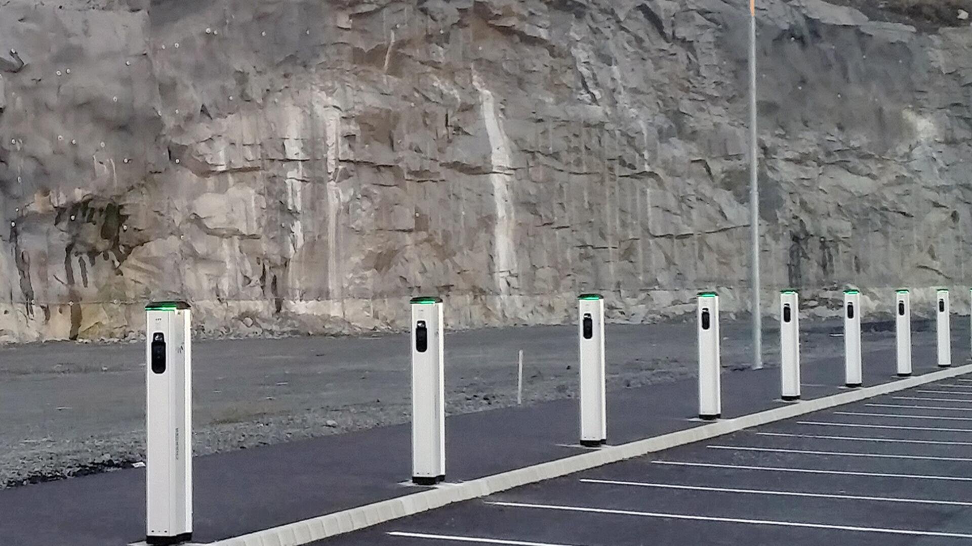 Eine Reihe von Ladestationen für Elektrofahrzeuge steht auf einem leeren Parkplatz an einer felsigen Klippe, ohne Autos und mit einer einzigen Straßenlaterne in Sichtweite.