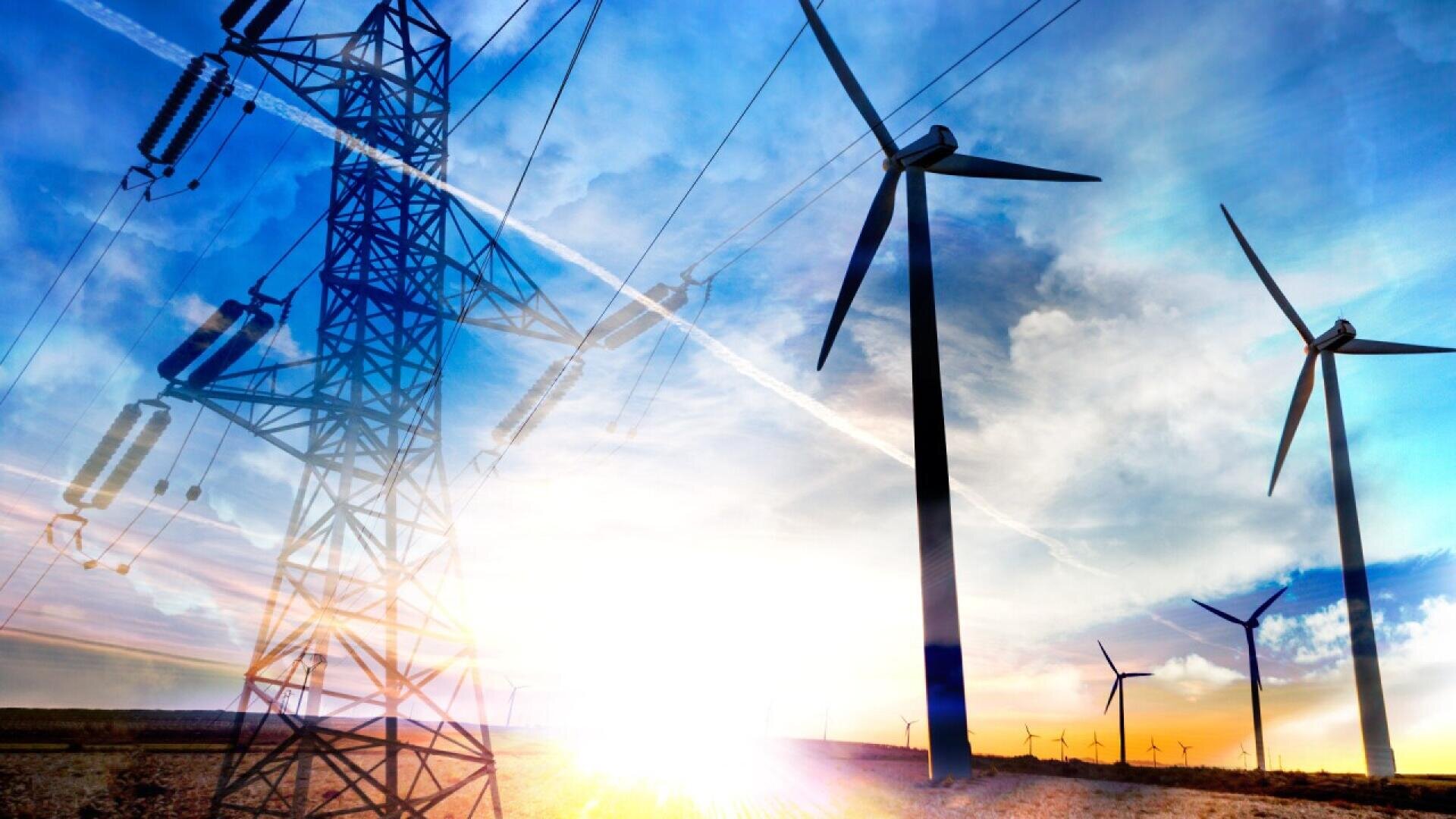 A field of wind turbines and an electricity transmission tower stand against a blue sky with clouds and sunlight, representing renewable energy and power generation.