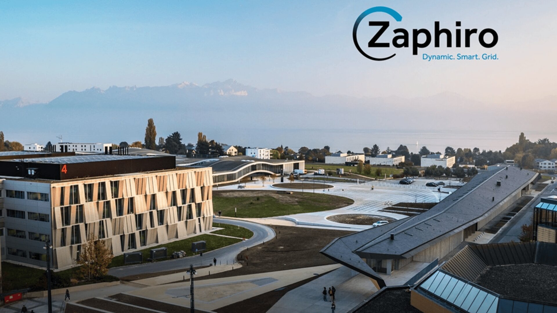 Ein moderner Universitätscampus mit geometrischen Gebäuden, Grünflächen und Wegen befindet sich in der Nähe eines großen Gewässers und von Bergen. Das Zaphir-Logo und der Slogan Dynamic. Smart. Grid. erscheinen am Himmel.