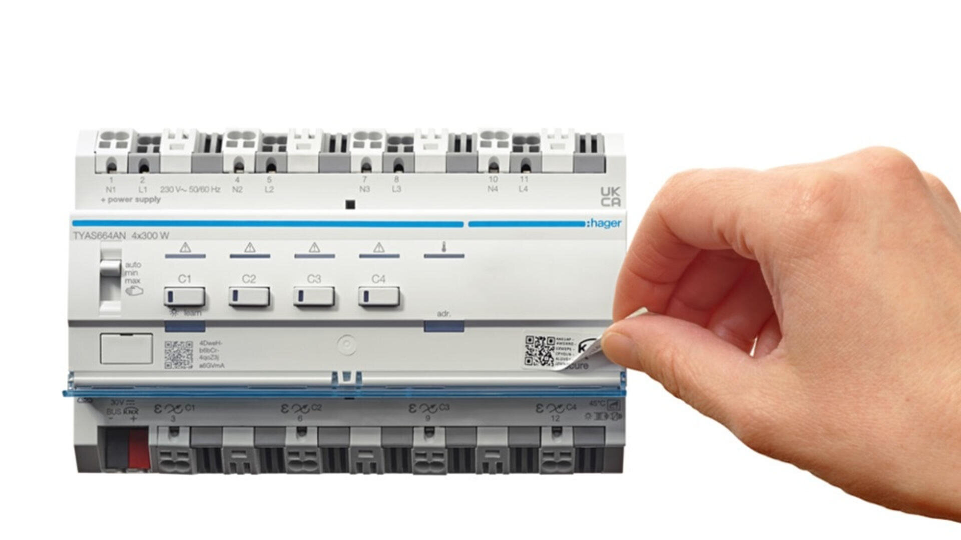 Eine Hand hält ein kleines Werkzeug in der Nähe eines weißen elektrischen Geräts mit mehreren Schaltern und Etiketten, darunter ein QR-Code. Das Gerät ist auf einer grauen Fläche montiert.