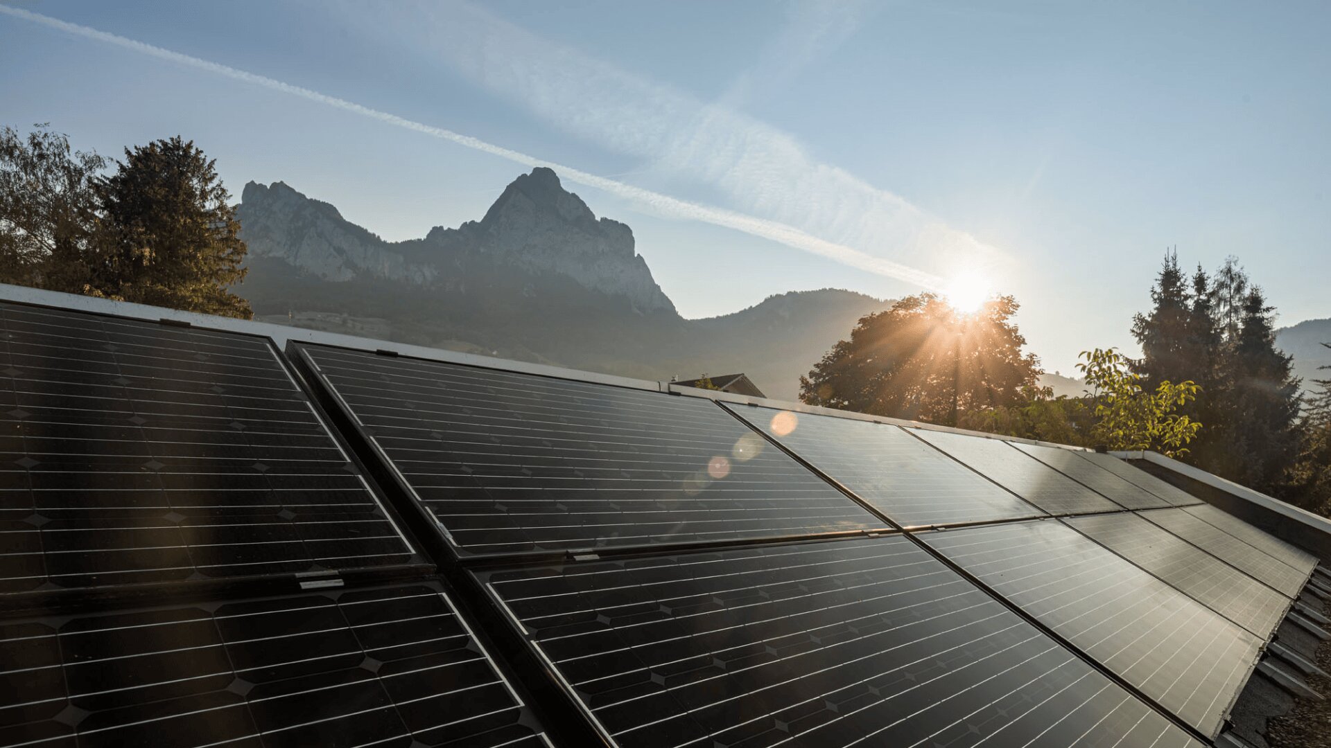 Solarmodule auf einem Dach reflektieren das Sonnenlicht mit einem malerischen Berg und Bäumen im Hintergrund, wenn die Sonne auf- oder untergeht und ein warmes Licht auf die Landschaft wirft.