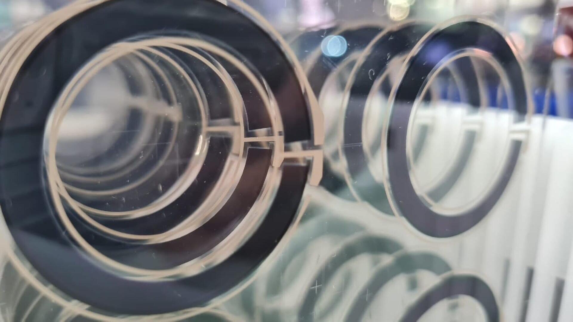 Nahaufnahme mehrerer transparenter Acrylscheiben mit schwarzen halbrunden Akzenten, die in parallelen Reihen angeordnet sind und einen tunnelförmigen visuellen Effekt mit Reflexionen und einem verschwommenen Hintergrund erzeugen.