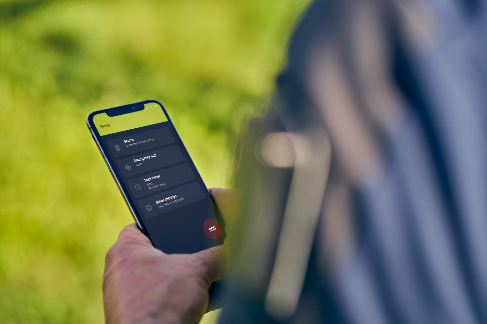 Eine Person, die im Freien ein Smartphone in der Hand hält und auf eine Aufgabenverwaltungs-App mit Optionen wie "Alle bezahlt", "Aufgabe erledigt" und "Andere Optionen" auf dem Bildschirm schaut. Der Hintergrund ist verschwommenes grünes Gras.