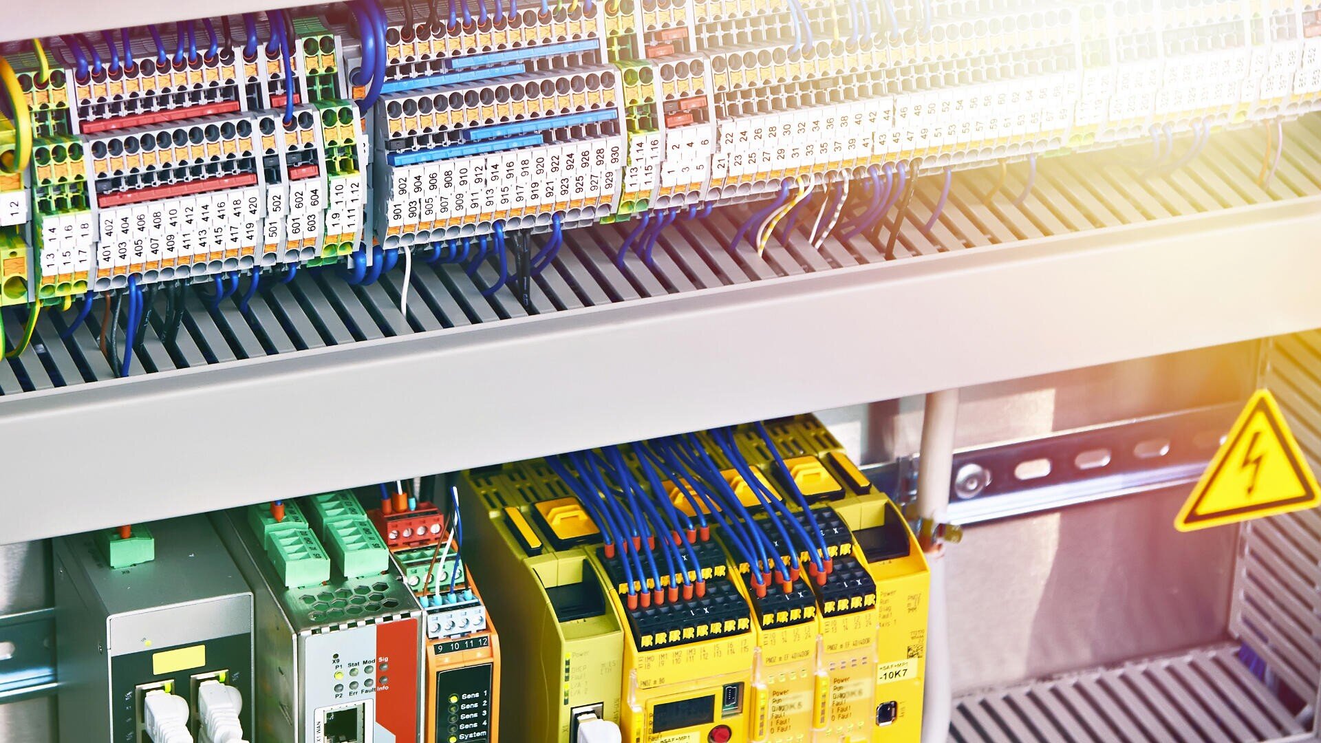 Ein industrieller elektrischer Schaltschrank mit Reihen von angeschlossenen Drähten, Klemmen und verschiedenfarbigen Komponenten, einschließlich gelber Sicherheitsrelais und Leiterplatten, innerhalb eines Metallgehäuses.