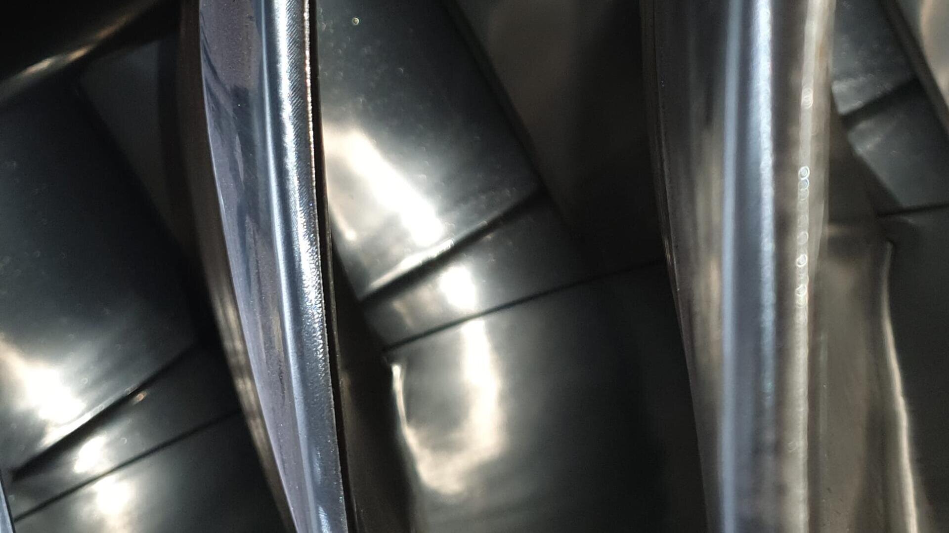 Nahaufnahme von glänzenden, schwarzen Metall- oder Kunststoffoberflächen mit geschwungenen und reflektierenden Linien, die ein abstraktes und industrielles Erscheinungsbild erzeugen. Licht und Schatten akzentuieren die glatte, glänzende Textur.
