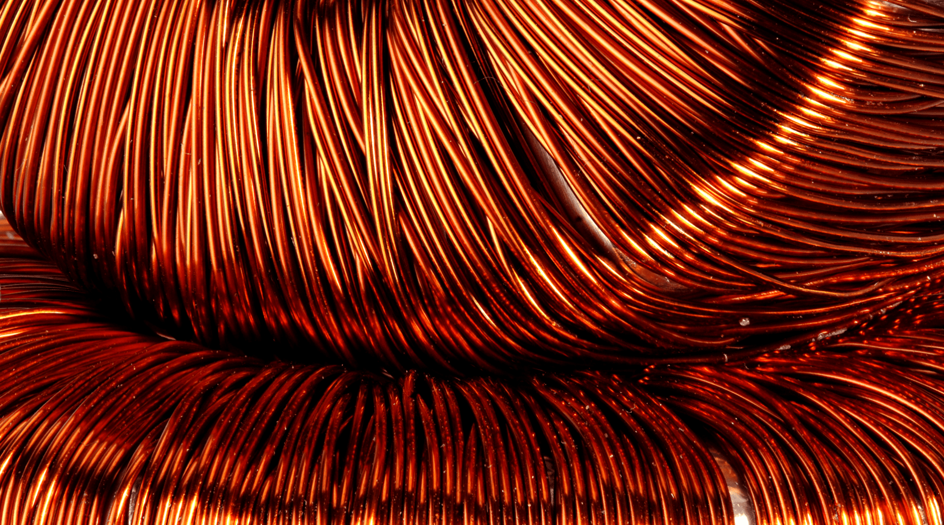 Close-up view of tightly coiled shiny copper wires, creating an intricate pattern with rich orange and metallic tones.