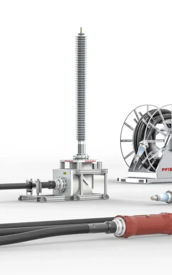 High-voltage electrical equipment with cables and connectors; a tall insulator stands upright beside a cable reel and additional power cables against a white background.