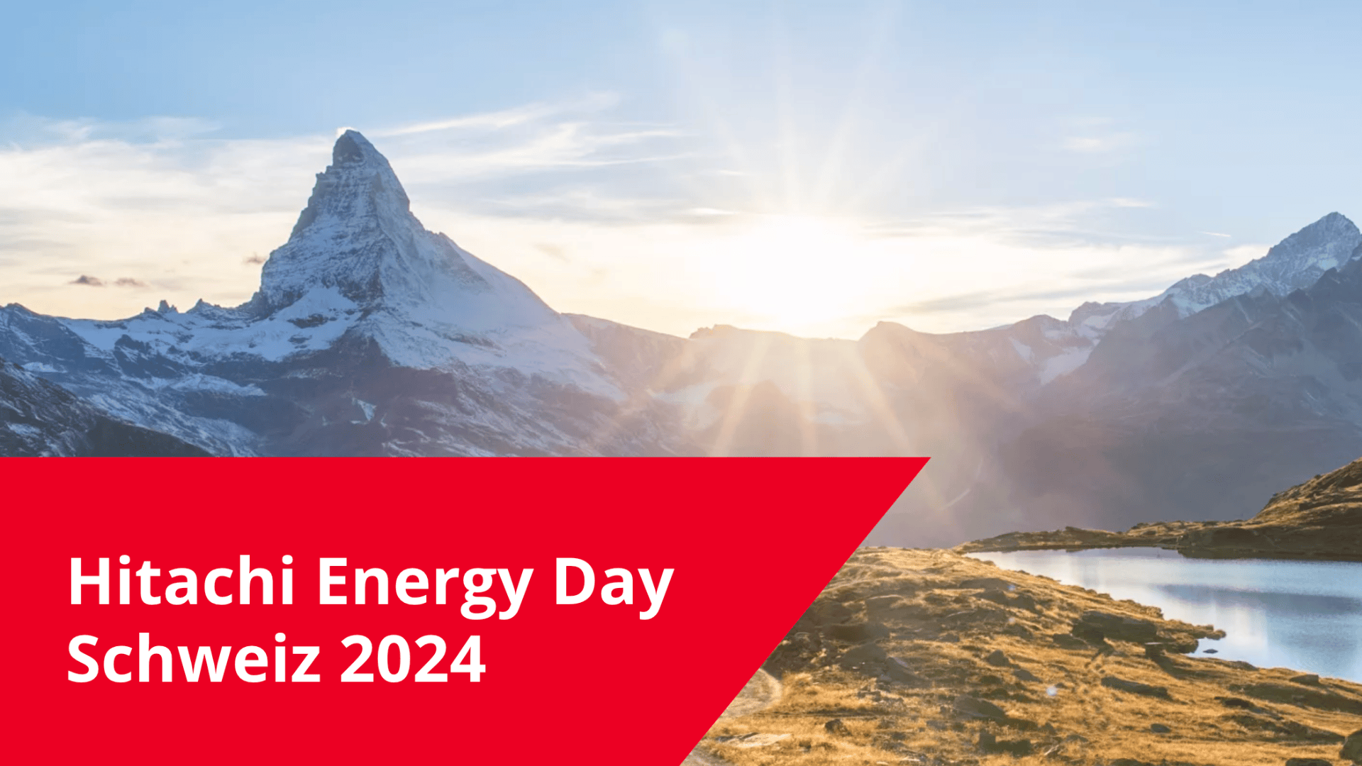 Schneebedeckte Berge bei Sonnenaufgang mit einem klaren See im Vordergrund. Auf einem roten Banner in der Ecke steht "Hitachi Energy Day Schweiz 2024".