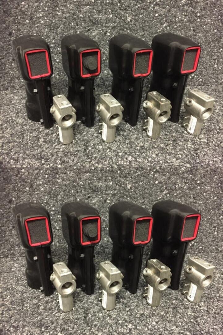 Vier schwarze Handgeräte mit roter Umrandung, jeweils mit einem kleinen silbernen Metallteil, sind in zwei identischen Reihen auf einer grau gesprenkelten Fläche angeordnet.
