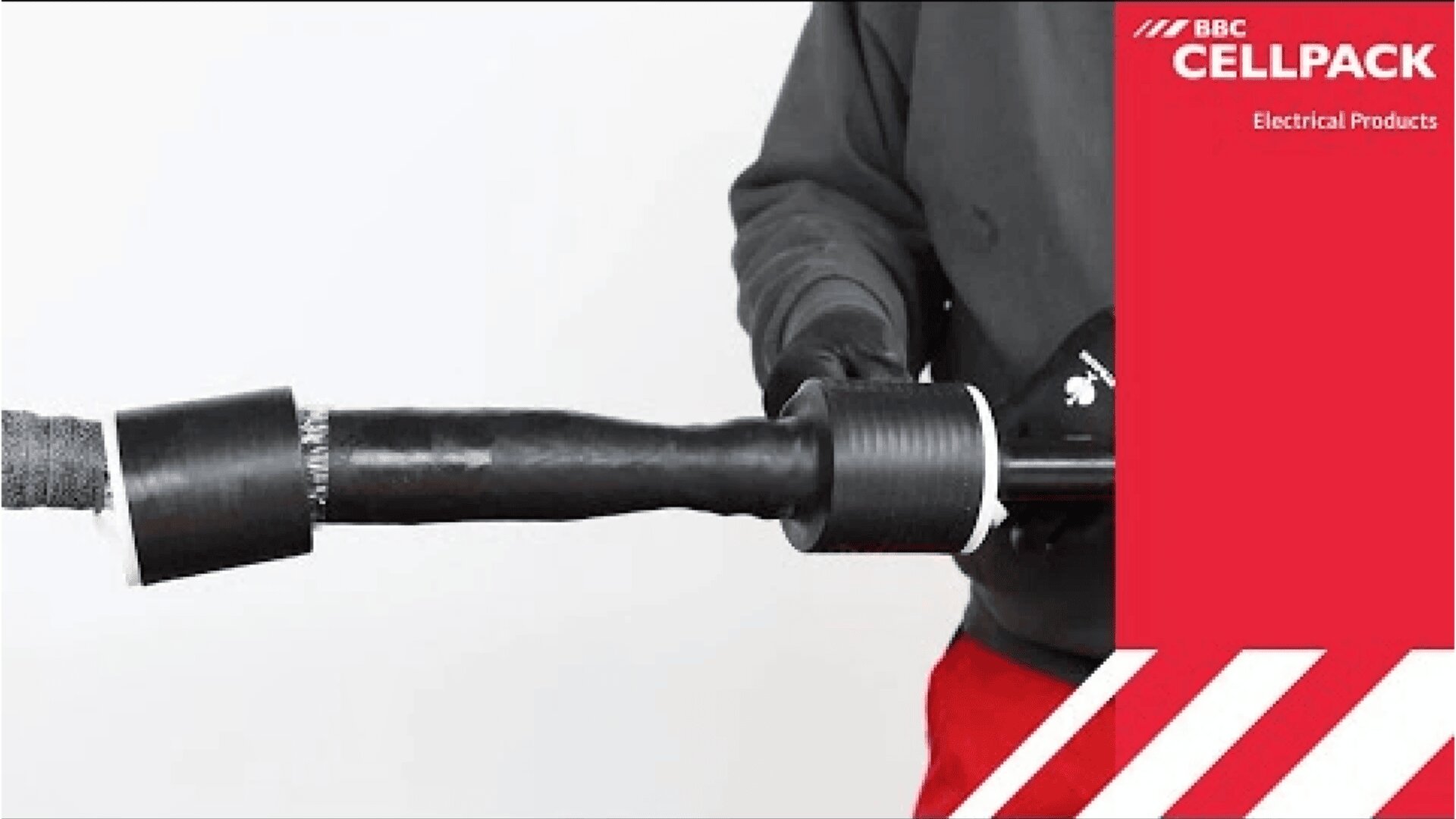 Eine Person bringt eine schwarze Isolierhülle an einem Kabel an, wobei das Branding von BBC Cellpack Electrical Products auf einer roten Tafel rechts zu sehen ist.