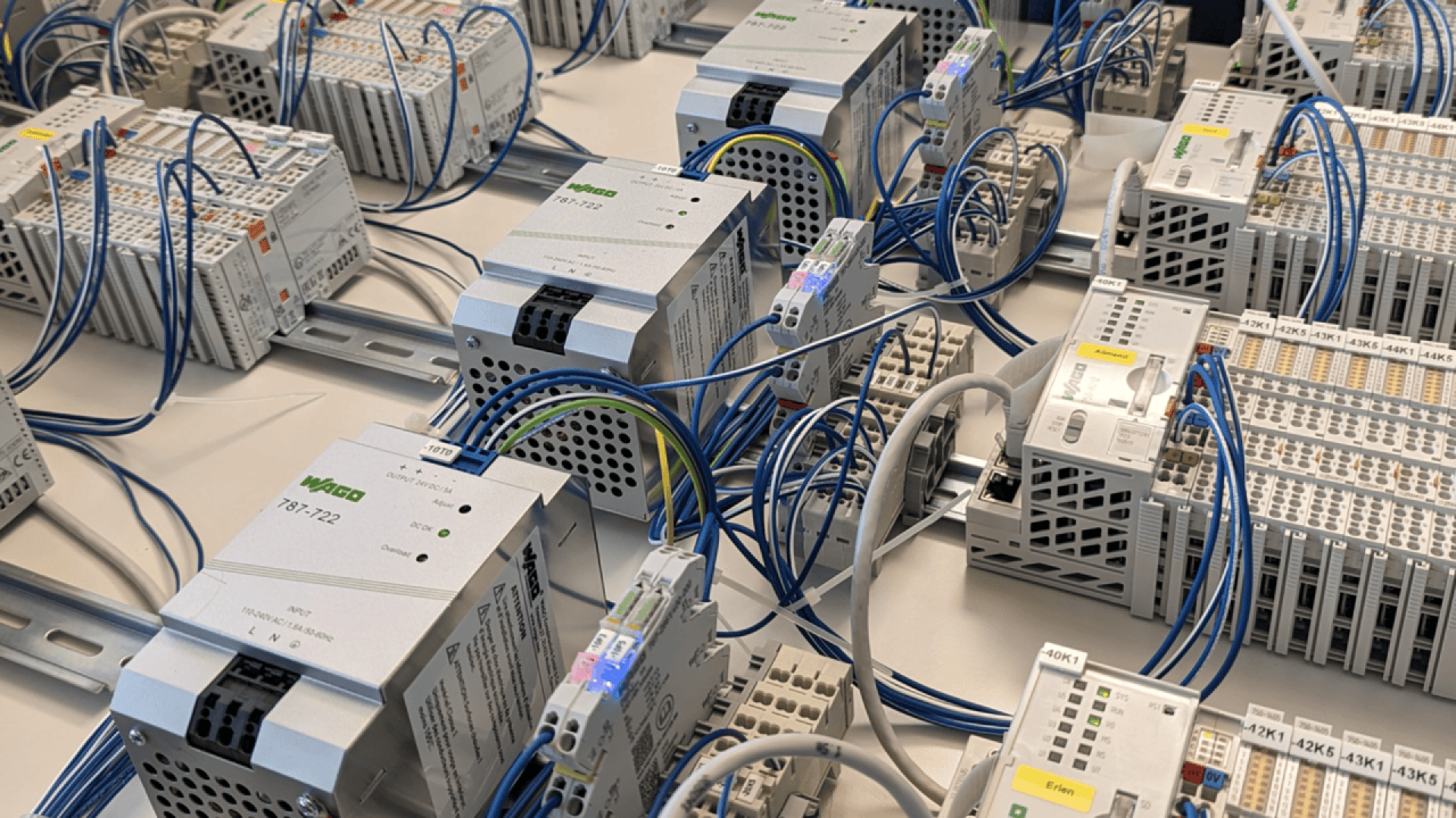 Close-up of an industrial control panel with multiple interconnected automation devices, terminal blocks, and blue signal wires, neatly organized on DIN rails in an electrical cabinet.
