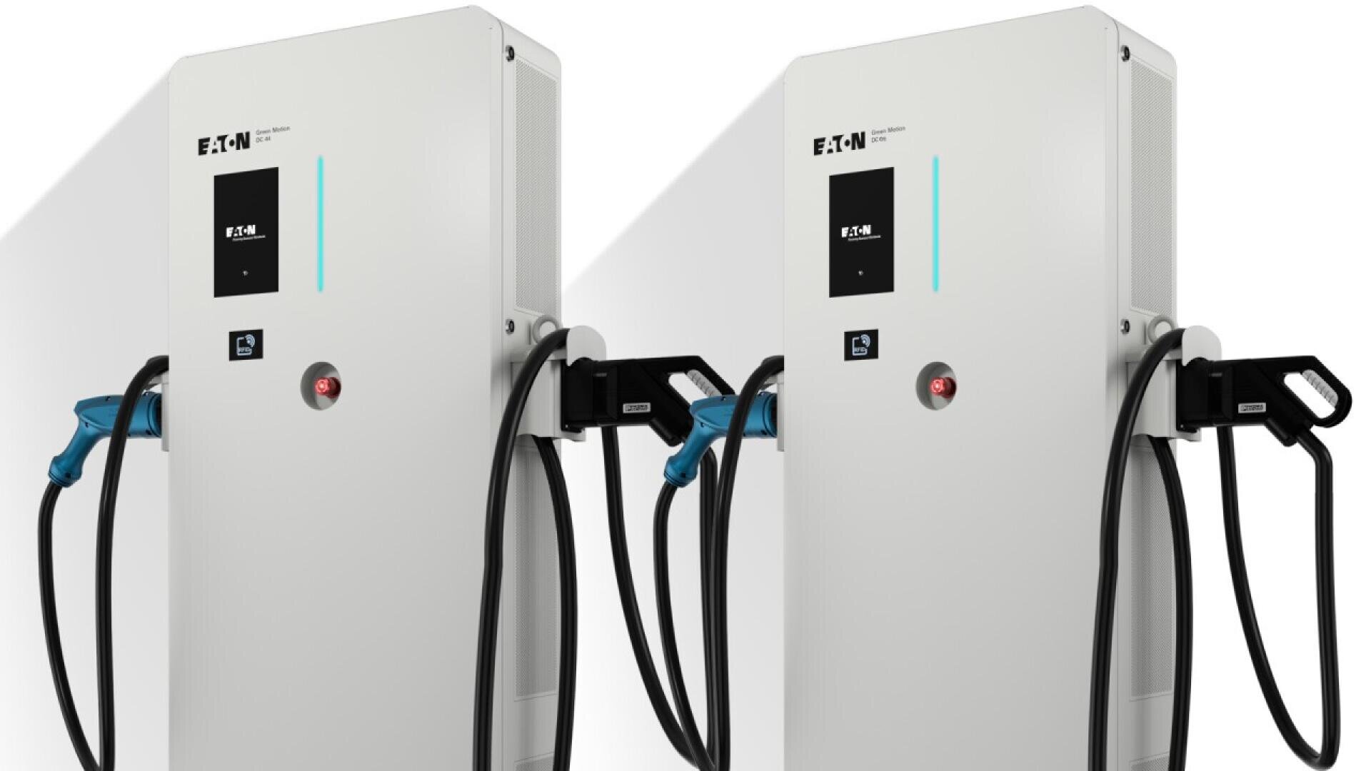Two white Eaton electric vehicle charging stations are positioned side by side, each with a screen, buttons, and attached black charging cables with blue-tipped connectors hanging on the side.