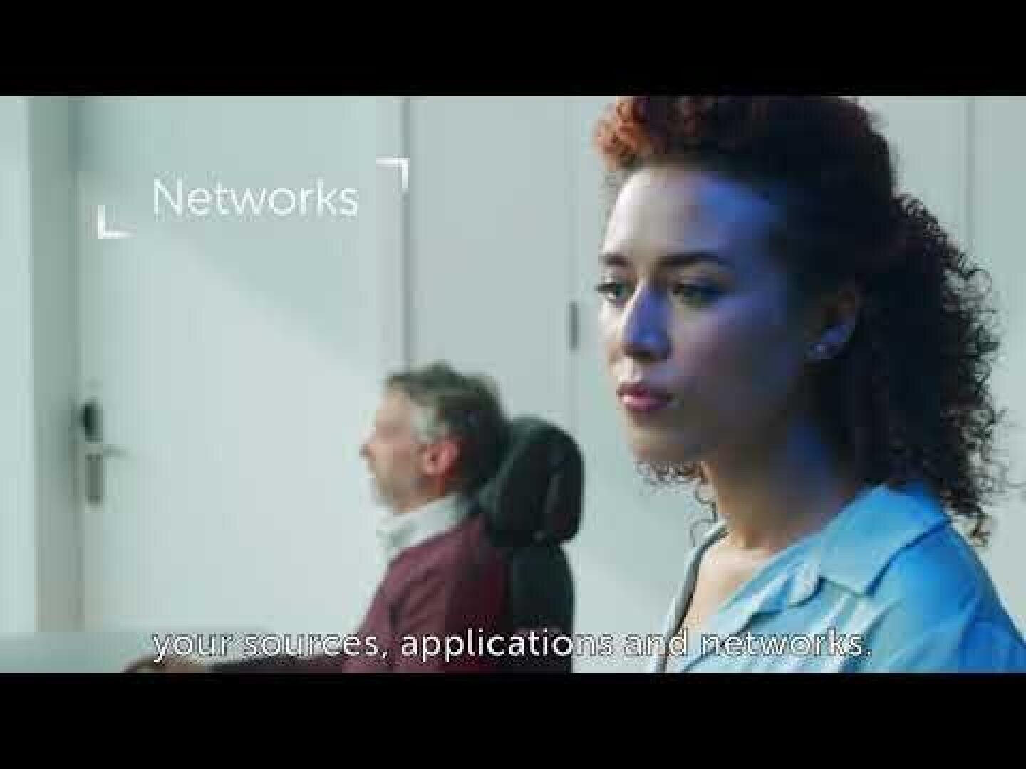 A woman with curly hair looks intently into the foreground while a man sits in the background. The word "Networks" appears on the screen, along with subtitles showing your sources, applications and networks.