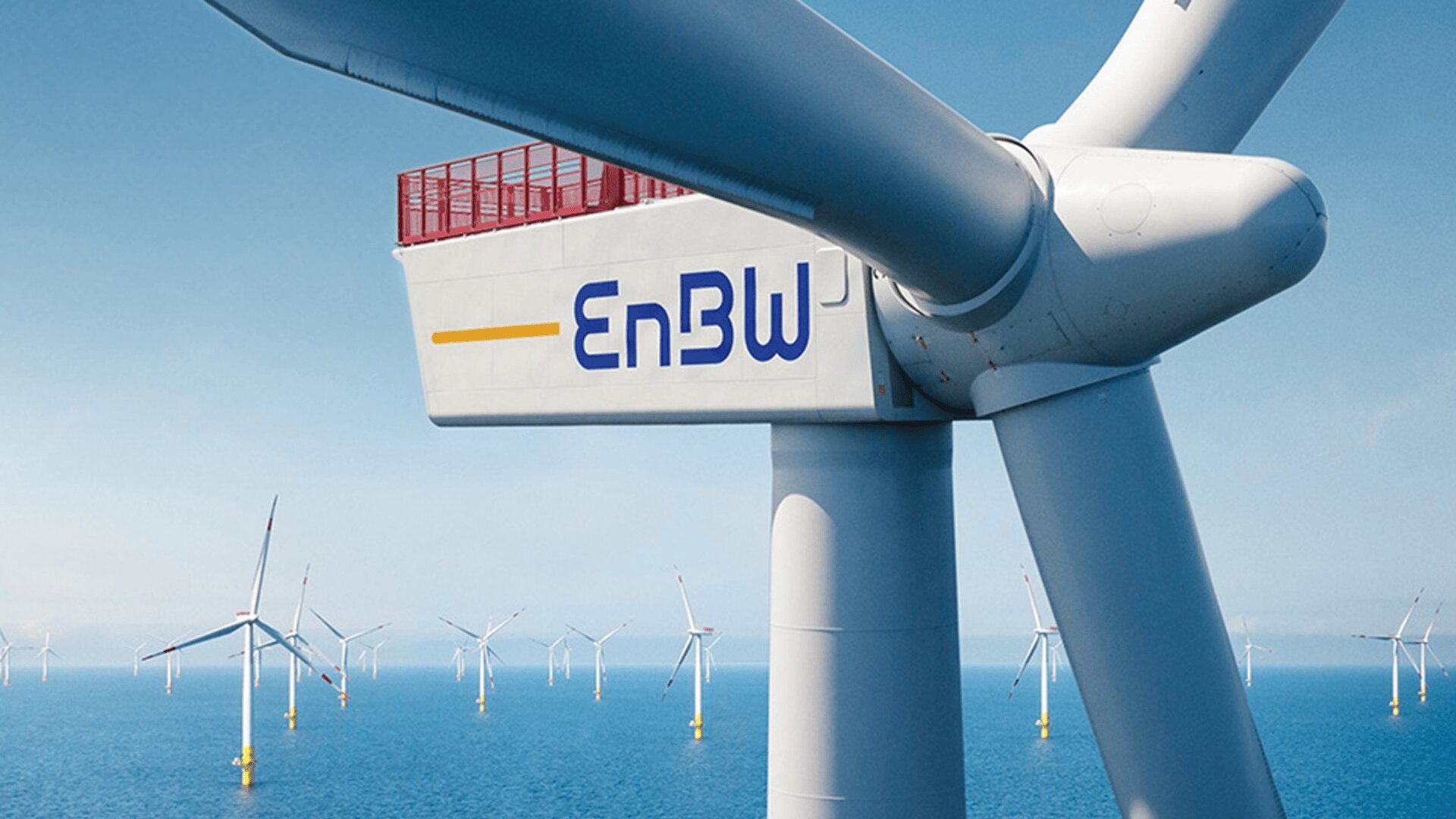 Nahaufnahme einer großen Offshore-Windturbine mit dem EnBW-Logo vor dem Hintergrund zahlreicher anderer Windturbinen, die unter einem klaren blauen Himmel im Meer stehen.