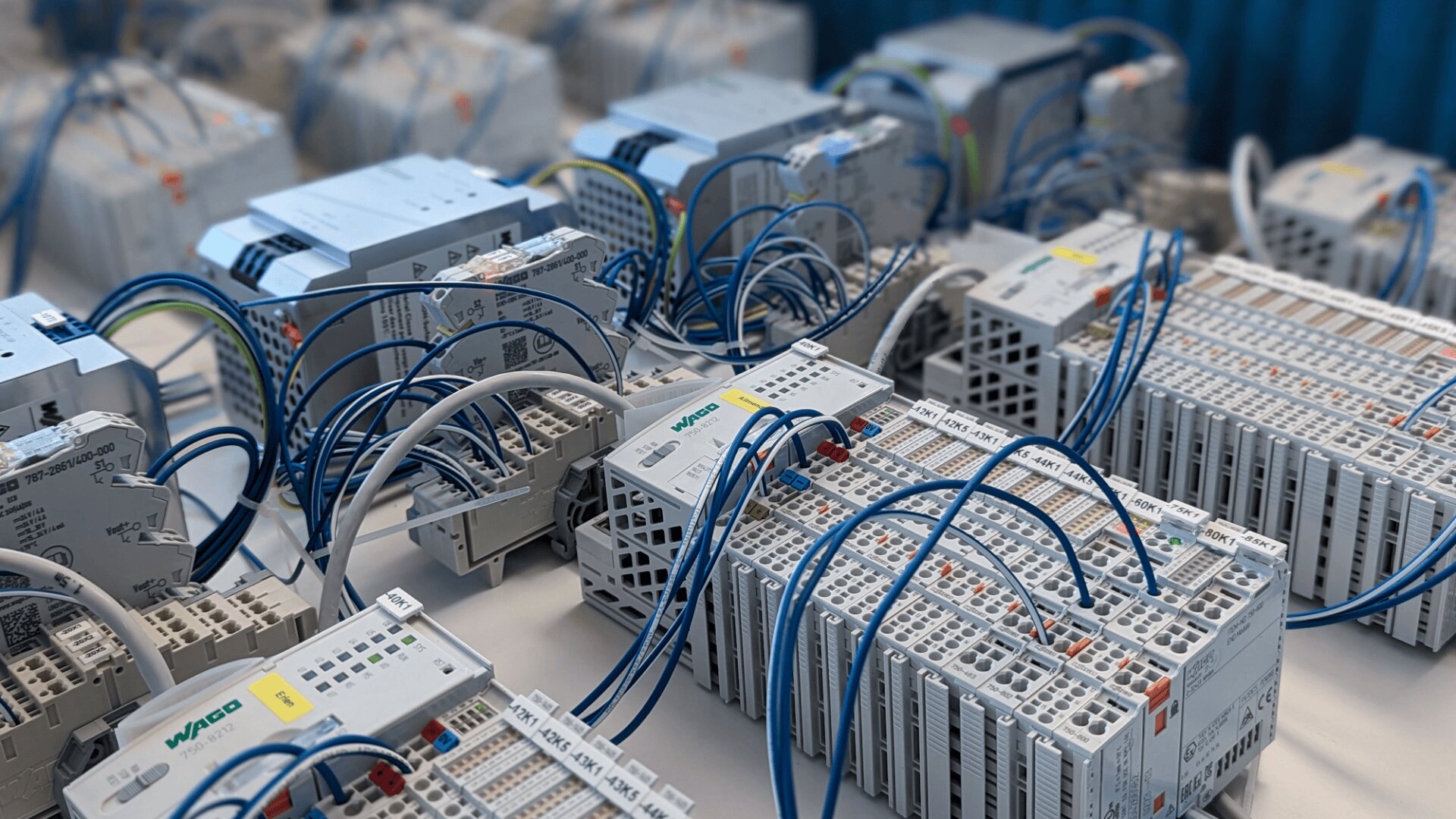 Mehrere industrielle speicherprogrammierbare Steuerungen (SPS) und Verdrahtungsmodule sind mit blauen Kabeln verbunden und auf einem Tisch in einer technischen oder Laborumgebung angeordnet.