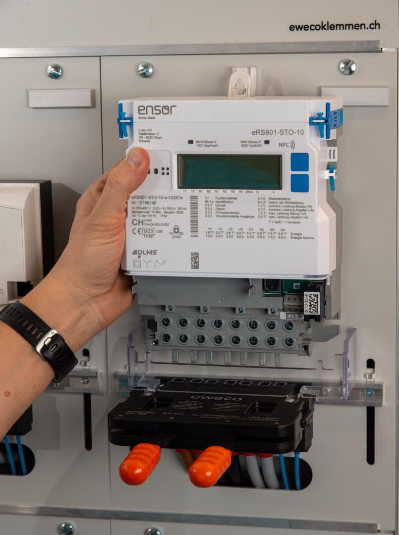 Eine Hand installiert einen digitalen Energiezähler mit der Bezeichnung ensor eRS801-STO-10 auf einer Schalttafel, mit sichtbarer Verkabelung und Steckern.