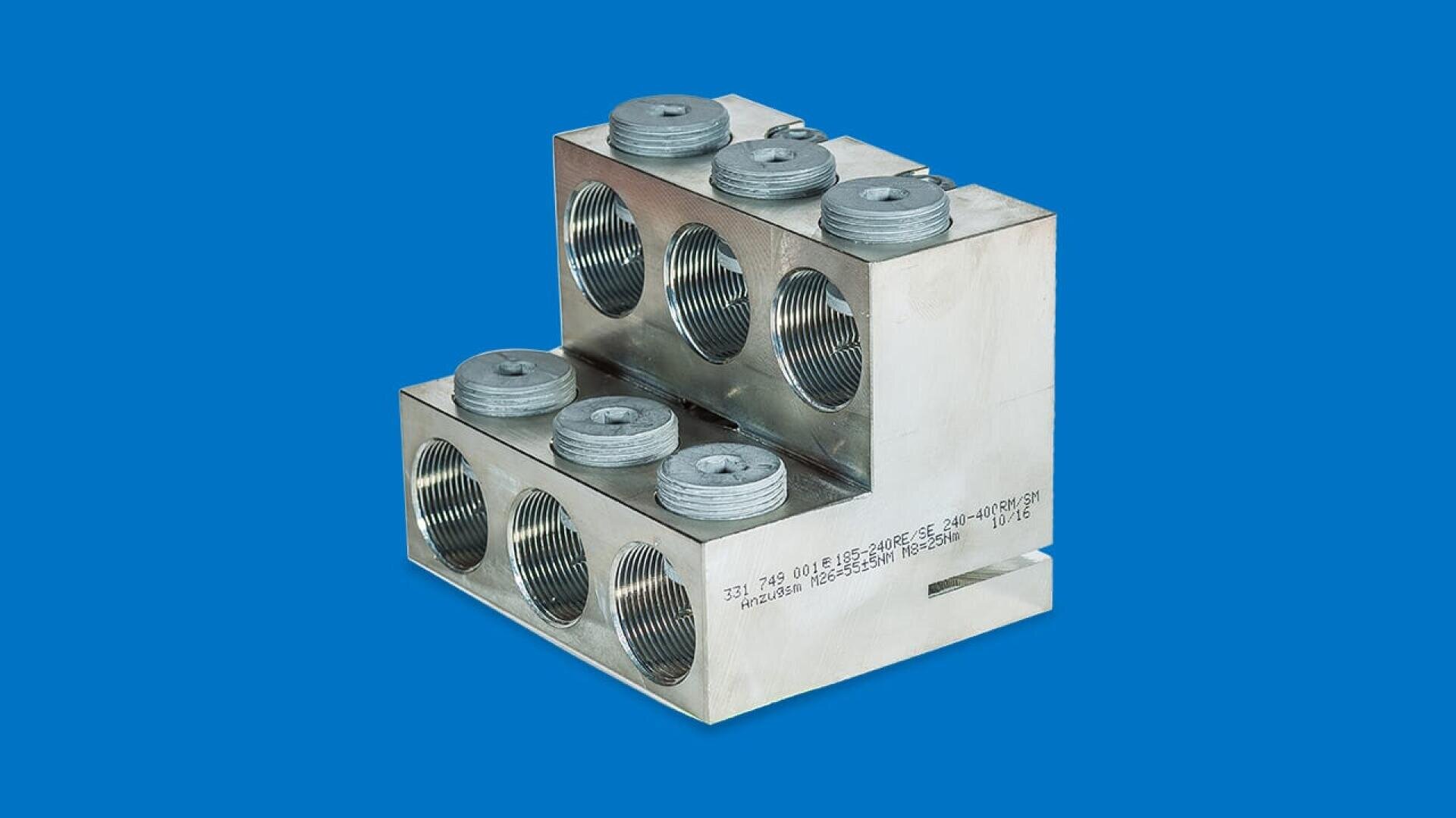 Ein rechteckiger metallischer elektrischer Anschlussblock mit mehreren Gewindelöchern und runden Kappen vor einem einfarbig blauen Hintergrund.