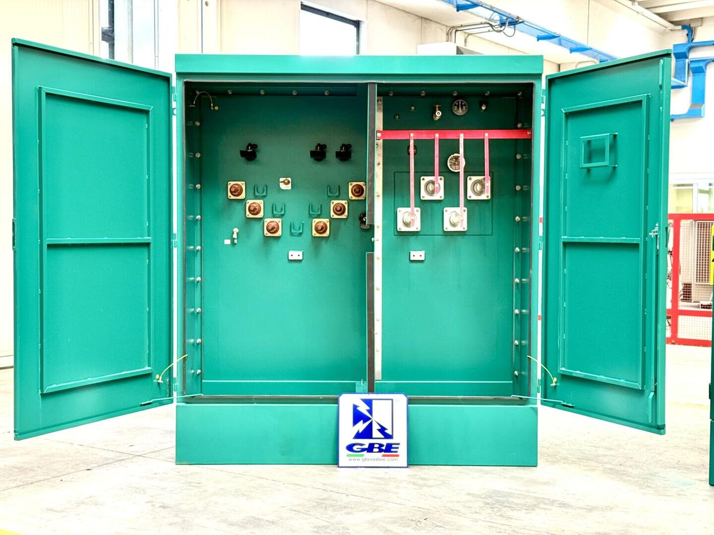 An open, teal green switch cabinet with two compartments and visible switches, fuses and diagnostic measuring devices. There is a GBE logo on the base.