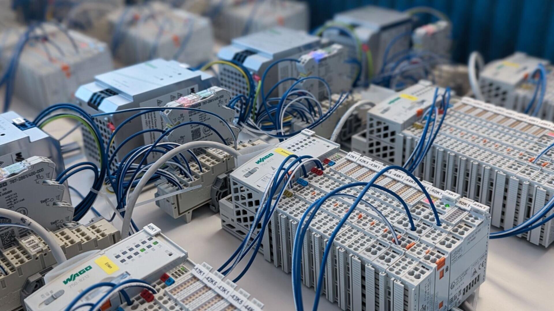 Several programmable logic controllers (PLCs) with numerous blue and white cables connected to terminals are arranged on a table in a technical or industrial setting.