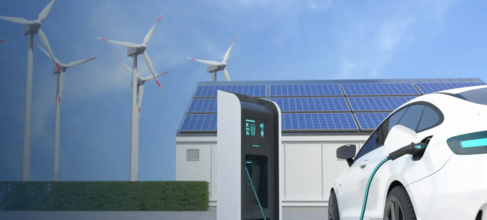 A white electric car charges at a station in front of a building with solar panels on its roof, while several wind turbines stand in the background under a clear blue sky.