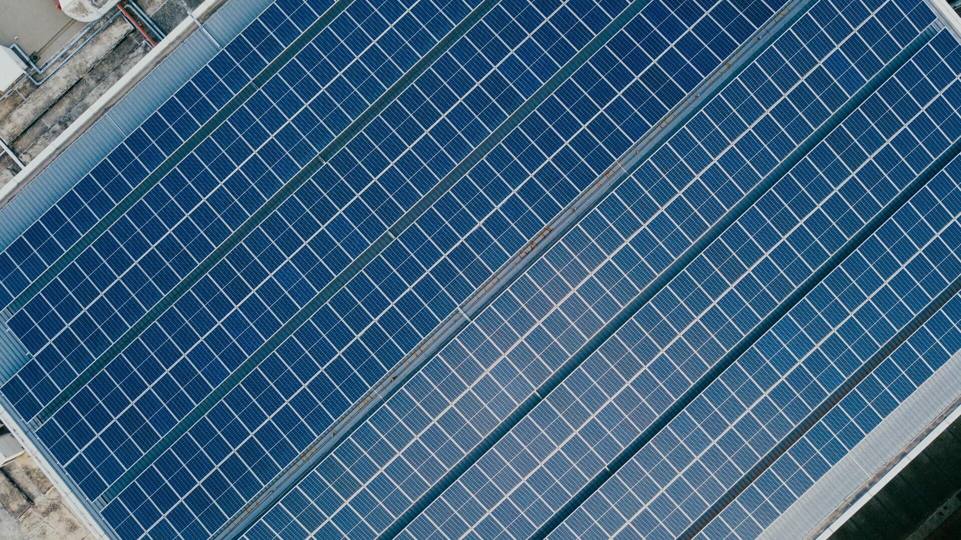Luftaufnahme von mehreren Reihen blauer Solarmodule, die auf einem Flachdach installiert und in parallelen Reihen angeordnet sind, um das Sonnenlicht zur Erzeugung erneuerbarer Energie einzufangen.