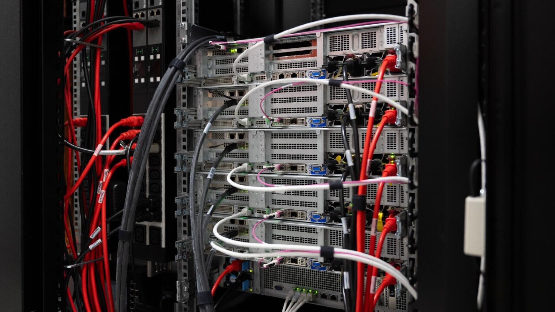 A close-up view of server racks filled with multiple servers connected by numerous red, black, and white network cables inside a data center.