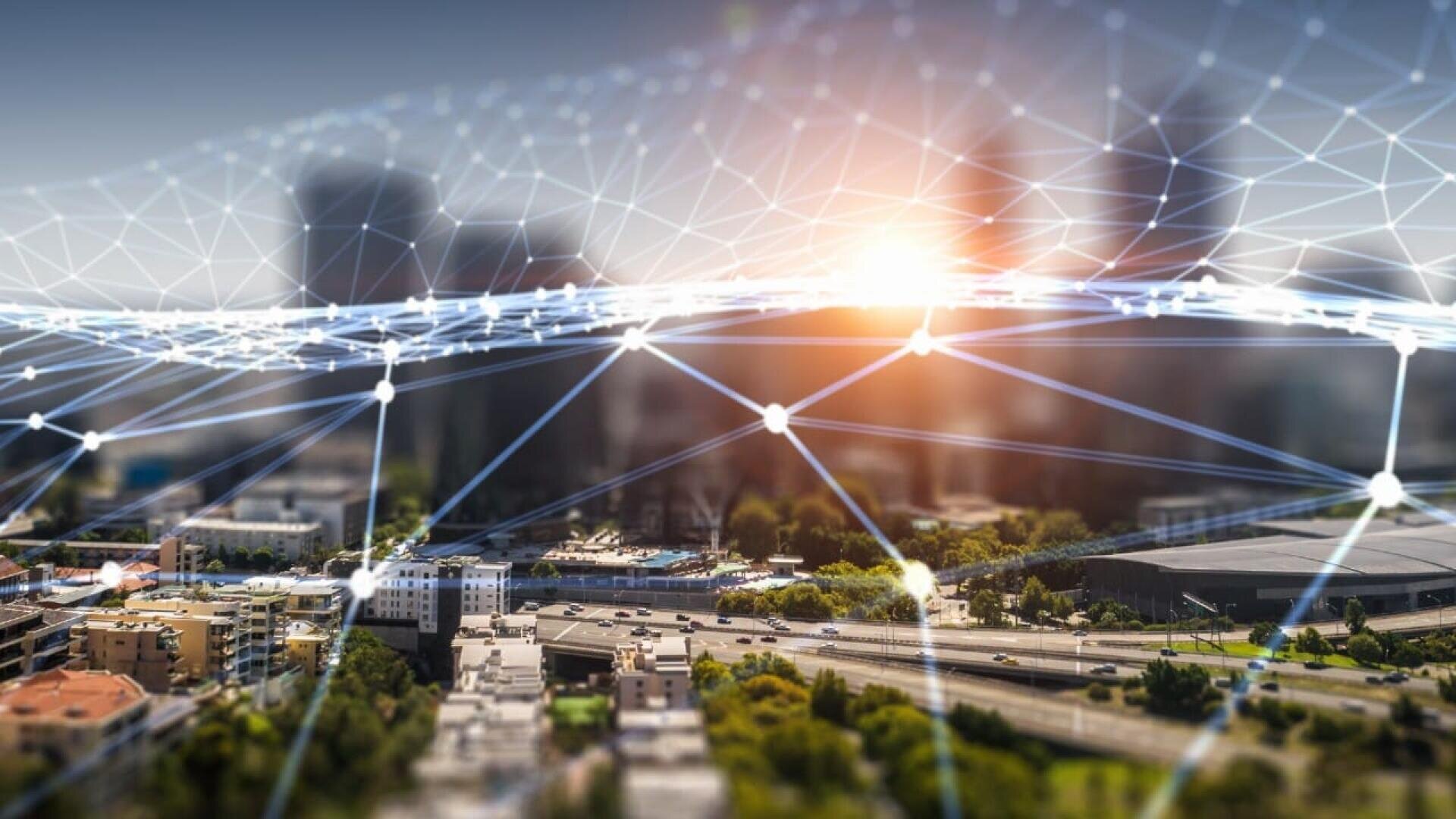 Eine Stadtlandschaft mit modernen Gebäuden im Sonnenlicht, überlagert von einem digitalen Netz aus miteinander verbundenen Linien und Knotenpunkten, die fortgeschrittene Konnektivität oder Smart-City-Technologie symbolisieren.