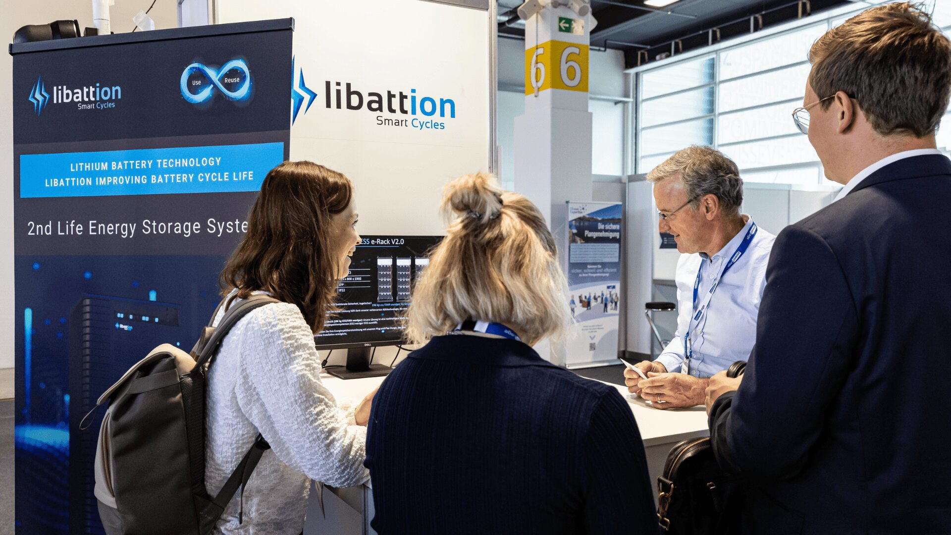 Vier Personen unterhalten sich an einem Stand von Libattion Smart Cycles auf einer Messe. Ein Banner zeigt Informationen über Lithium-Batterietechnologie und Energiespeichersysteme der zweiten Generation.