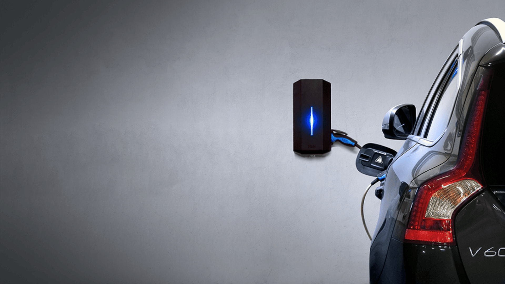 Ein schwarzes Elektroauto wird aufgeladen, eingesteckt in eine an der Wand montierte Ladestation mit blauem Licht, vor einem schlichten grauen Hintergrund.