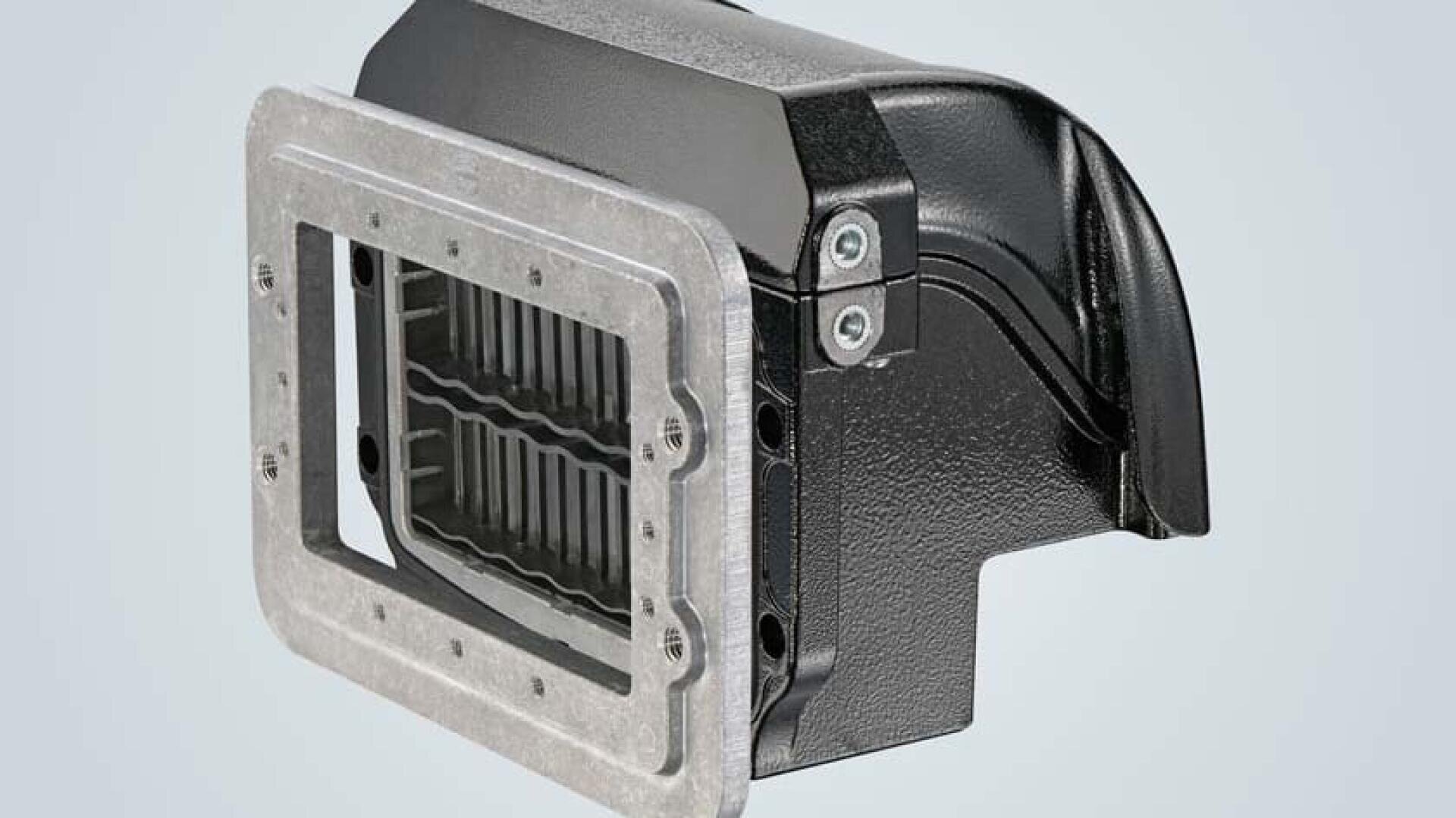 A close-up view of a black and silver metal machine component with a rectangular opening and ribbed interior, secured by screws, against a light gray background.