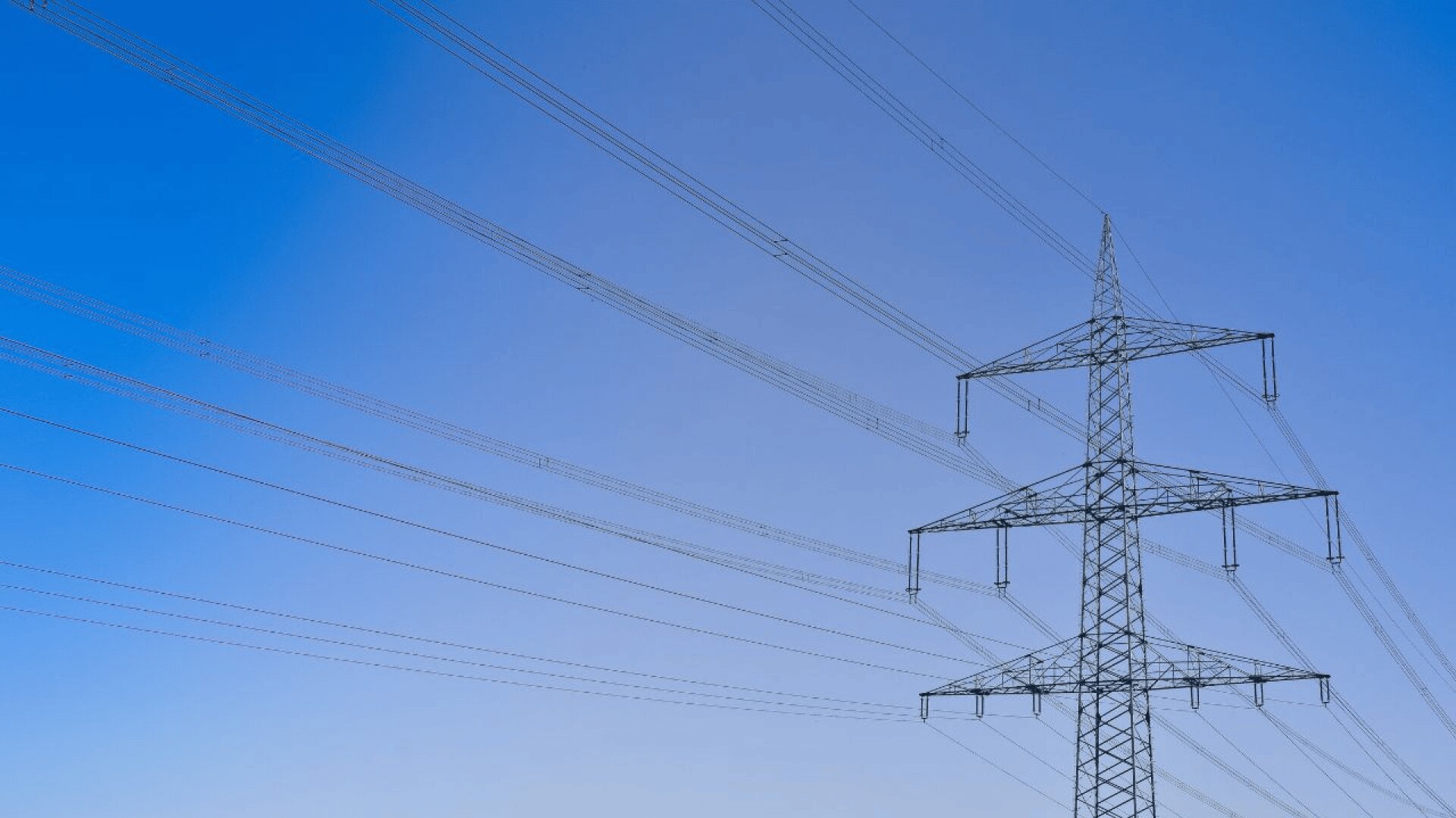 Ein hoher Hochspannungsmast mit mehreren Drähten ragt in den blauen Himmel und veranschaulicht die elektrische Infrastruktur.