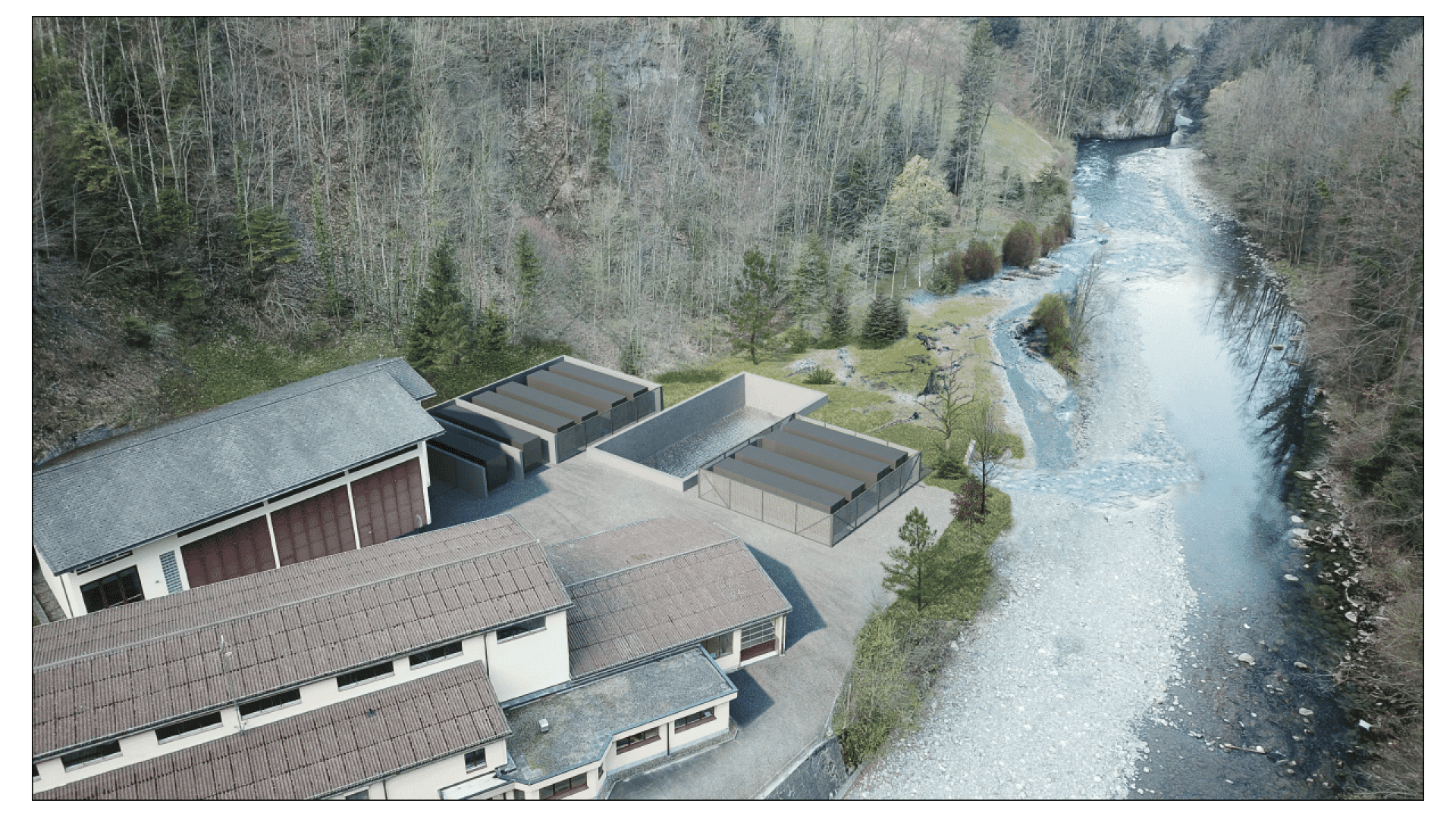 Luftaufnahme einer Industrieanlage am Flussufer mit mehreren rechteckigen Gebäuden und Außenanlagen, die von Bäumen umgeben sind und von einem gewundenen Fluss und einem felsigen Ufer begrenzt werden.