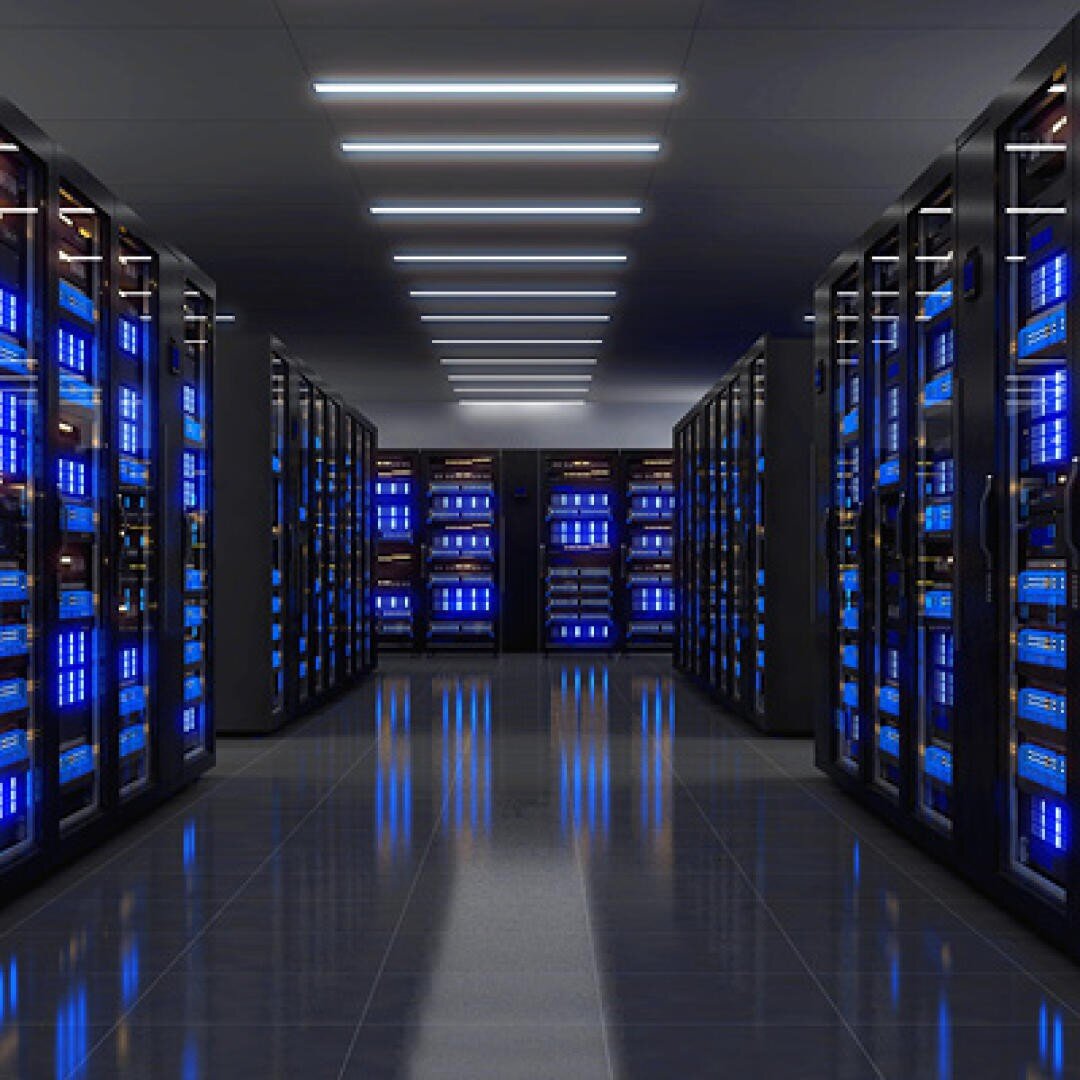 A modern data center with rows of black server racks, each equipped with glowing blue devices. The glossy floor mirrors the racks and strip lighting overhead, creating a clean, high-tech environment.