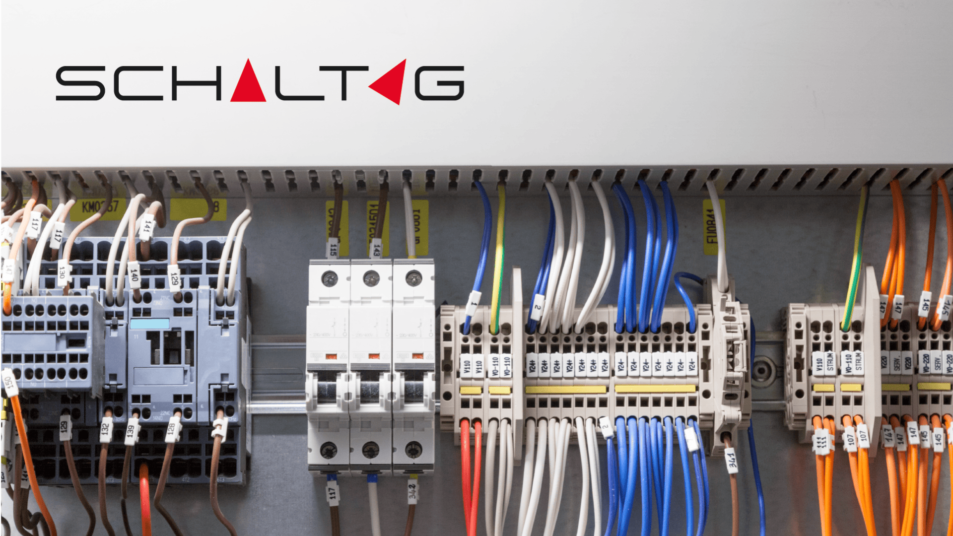 Eine elektrische Schalttafel mit verschiedenfarbigen Drähten, die mit Leistungsschaltern und Klemmen verbunden sind. Das Wort SCHALTAG ist in fetten Buchstaben auf der weißen Abdeckung der Schalttafel zu sehen.
