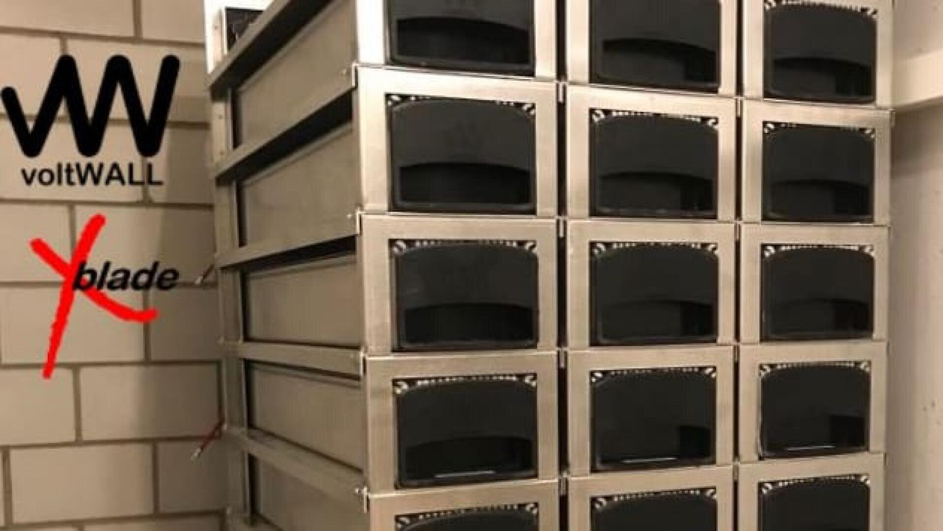 A stack of metal battery modules is mounted against a tiled wall. The voltWALL logo appears in the top left, and the word blade is crossed out in red beneath it.