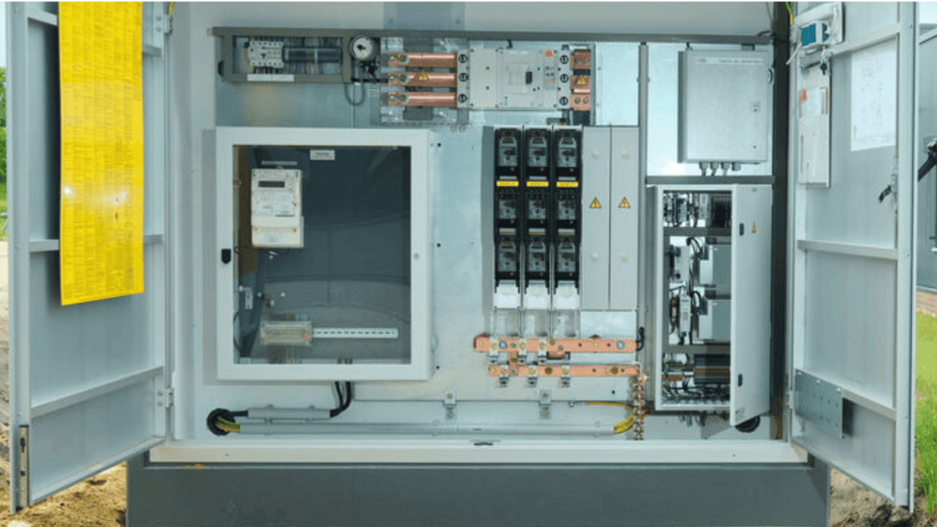 An open electrical control cabinet displaying circuit breakers, wiring, switches, meters, and electrical components organized in metal enclosures and panels.