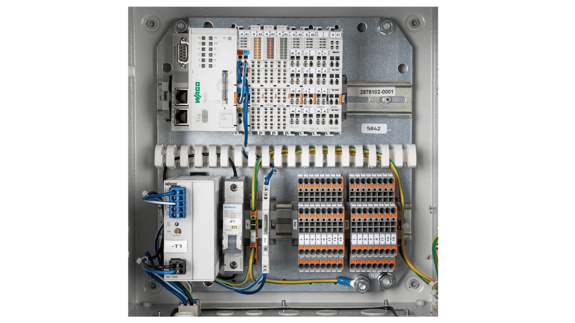 Eine elektrische Schalttafel mit verschiedenen Kabeln, Leiterplatten, Klemmenleisten, Relais und beschrifteten Anschlüssen, die übersichtlich in einem Metallgehäuse angeordnet sind. Die farbigen Drähte sind geordnet und zu den verschiedenen Komponenten verlegt.