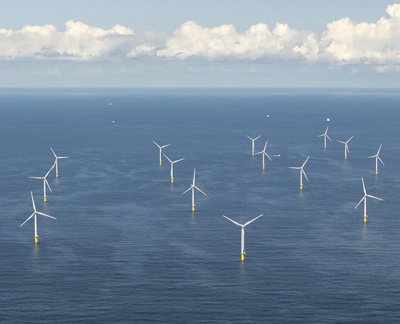 Aerial view of multiple wind turbines spread across the ocean, generating renewable energy under a partly cloudy sky.