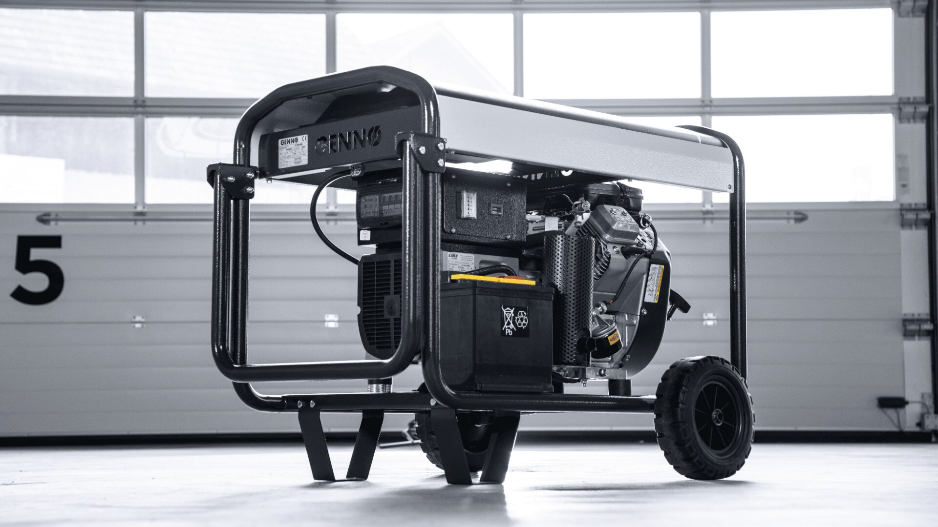 Ein tragbarer Generator mit schwarzem Gestell und Rädern steht auf einem glatten Boden in einer Garage, in der Nähe einer weiß getäfelten Tür mit der Nummer 5 im Hintergrund.